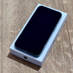 New iPhone in its white box lies on a wood surface, screen off and facing up.
