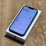 New iPhone in its white box resting on a wooden surface, screen showing the Settings menu in Polish.