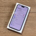 New iPhone in its white box on a wooden table, screen showing Settings in Polish with network options visible to the user.