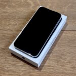 Black smartphone with screen off placed on top of its white retail box on a wooden table surface.