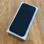 Black smartphone with a dark screen lying diagonally on a white box atop a wooden surface.