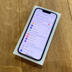 New iPhone in a box on a wooden table, screen shows Polish Settings app.