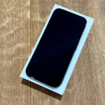 Smartphone with a black screen resting on its white box on a wooden table, photographed at an angle.