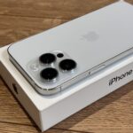 White iPhone with a triple-lens rear camera system resting on its box on a wooden surface, Apple logo visible