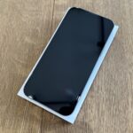 Black smartphone with a nearly bezel-free screen lying face up on a white box on a wooden surface.