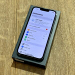 Nowy iPhone w czarnym pudełku leży na drewnianym blacie, wyświetla ekran Ustawień Apple (Ustawienia).