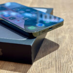 Close-up of a smartphone resting on its box on a wooden table, screen showing app icons and colorful UI.