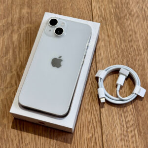 Silver iPhone in its box on a wooden surface with a coiled white charging cable beside it.