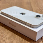White iPhone resting on its box on a wooden surface, with side buttons visible along the edge.
