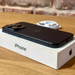 Black iPhone with triple-camera system lying on its white box on a wooden table.