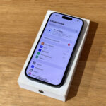 New Apple iPhone in its white box on a wooden table, displaying the Polish Settings app on the screen (Ustawienia).