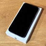 Black iPhone with screen off resting on its white box on a wooden table surface