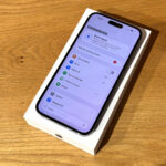 New iPhone in its white box resting on a wooden table, screen showing the Polish Settings app (Ustawienia).