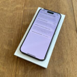Smartphone on a white box resting on a wooden table, screen showing battery settings in Polish.