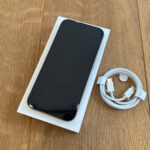 New smartphone in white box on a wooden surface, with a white charging cable nearby.
